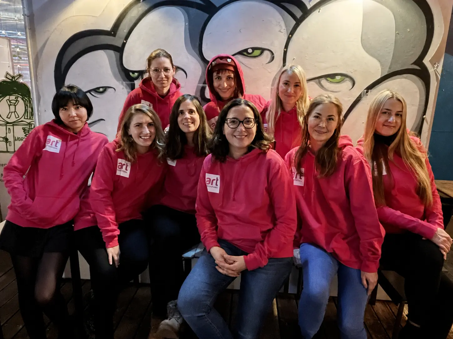 Das Team von Art Adventure in pinken Hoodies vor einer Graffiti-Wand